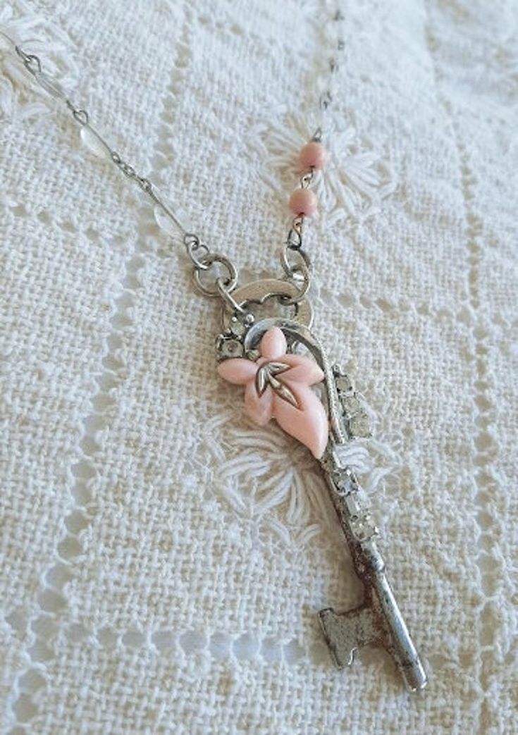 a necklace with pink flowers on it and a key hanging from the chain that is attached