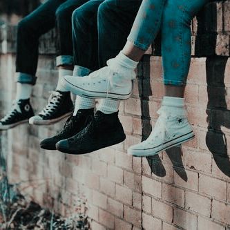 four people sitting on a brick wall with their feet hanging off the ledge and wearing converse shoes