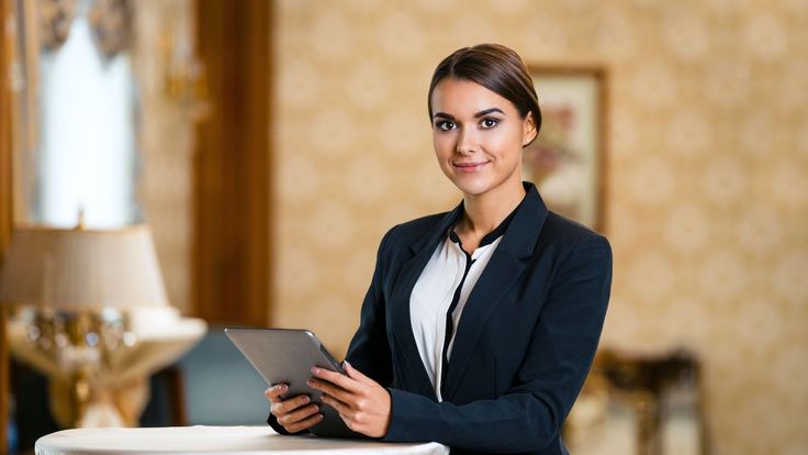 a woman standing next to a table with a tablet computer in her hand and looking at the camera