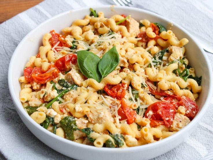 a white bowl filled with pasta and spinach on top of a table next to a fork