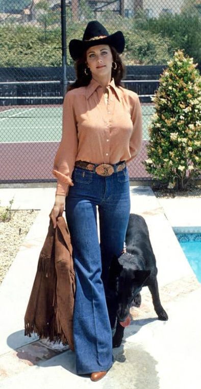 a woman in jeans and a cowboy hat standing next to a black dog