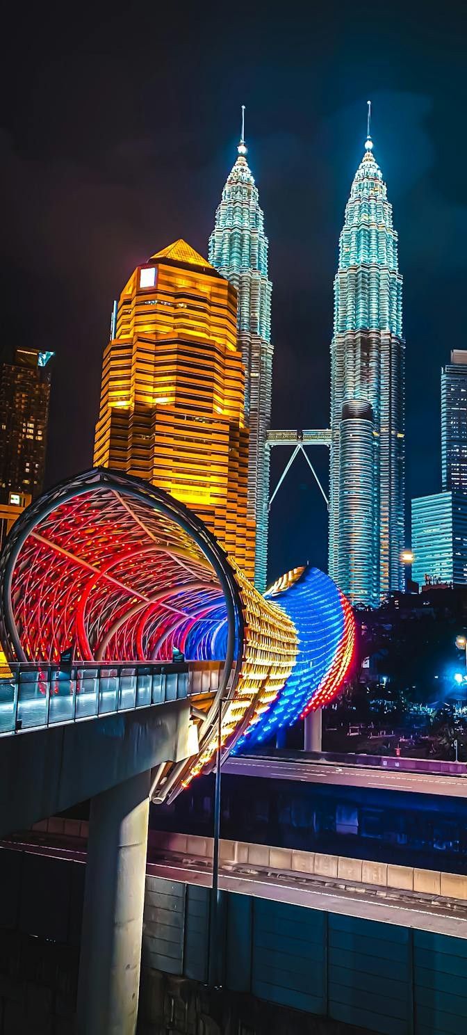 the city skyline is lit up at night with colorful lights and skyscrapers in the background