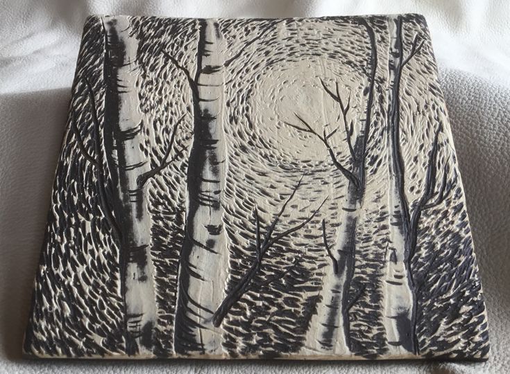 a small wooden box with trees painted on the front and sides, sitting on a bed