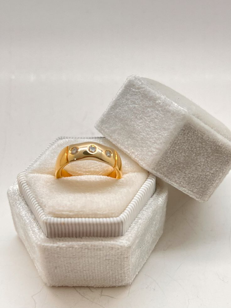 an open ring box with a gold wedding band in it's packaging on a white surface