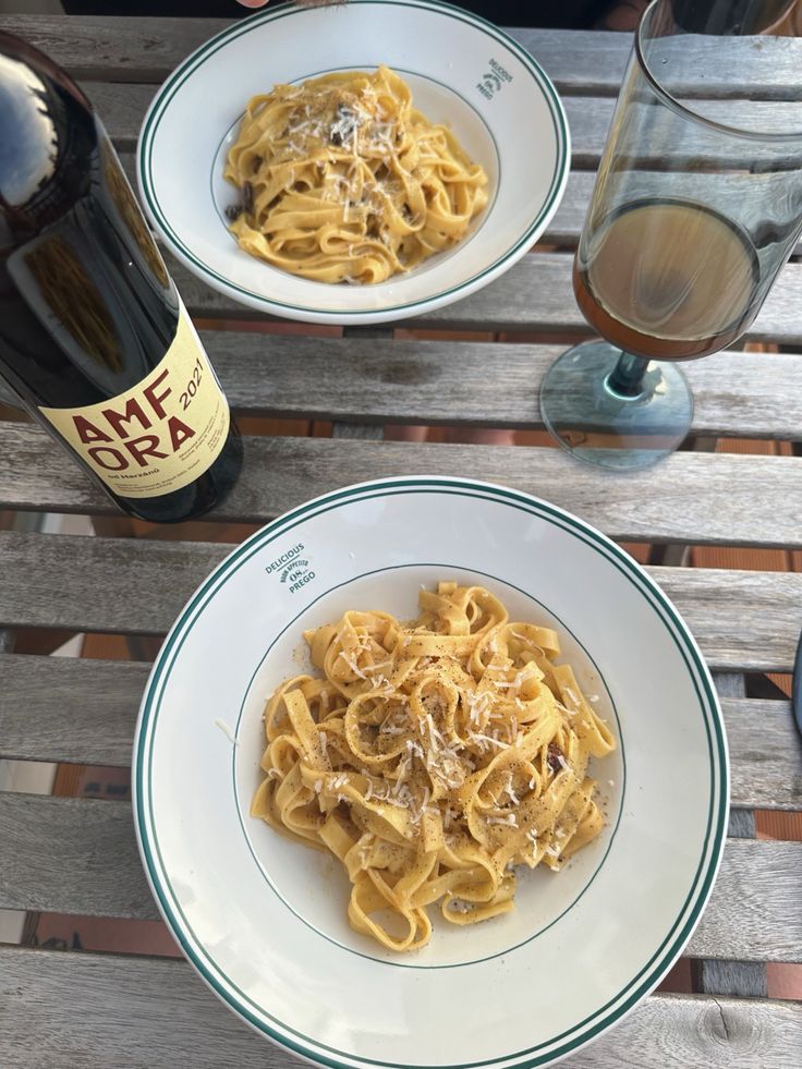 two plates of pasta and wine on a wooden table