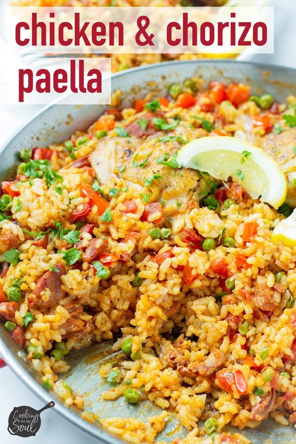 chicken and chorizo paella in a skillet with lemon wedges on the side