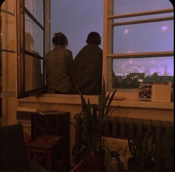 two people are sitting on a window sill looking out at the city below them