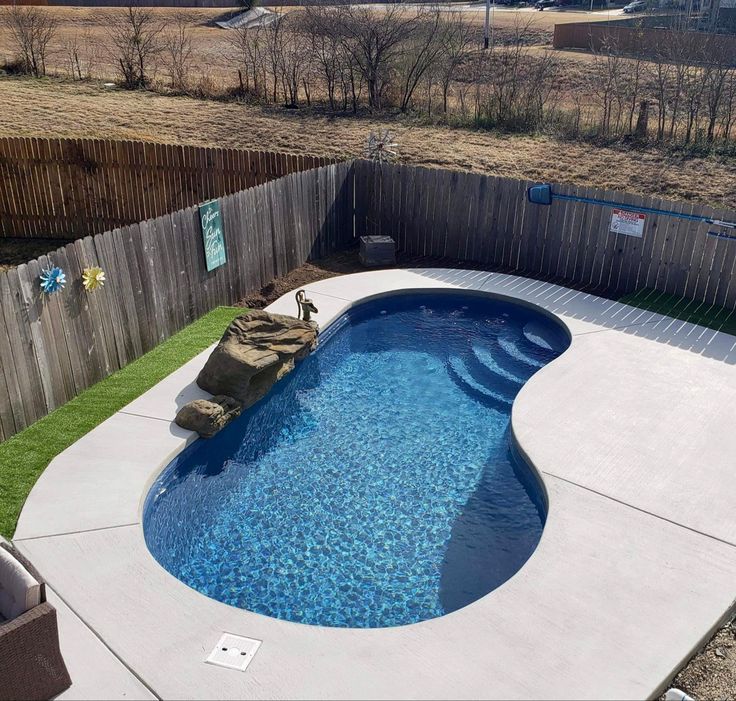 an above ground swimming pool surrounded by a wooden fence and grass area with rocks on the edge