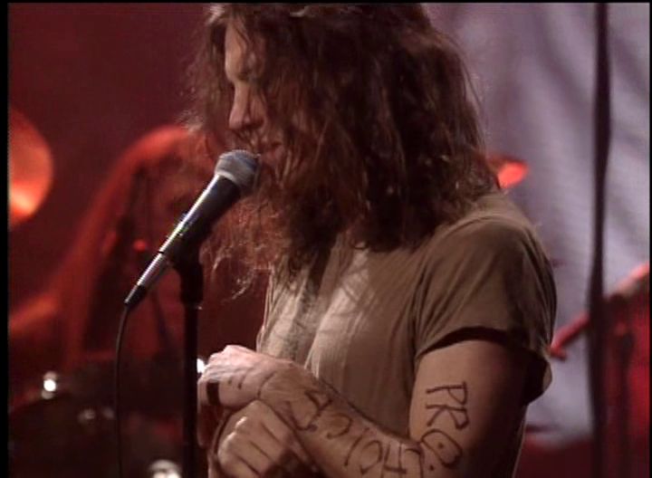 a man with long hair and tattoos on his arm holding a microphone in front of him