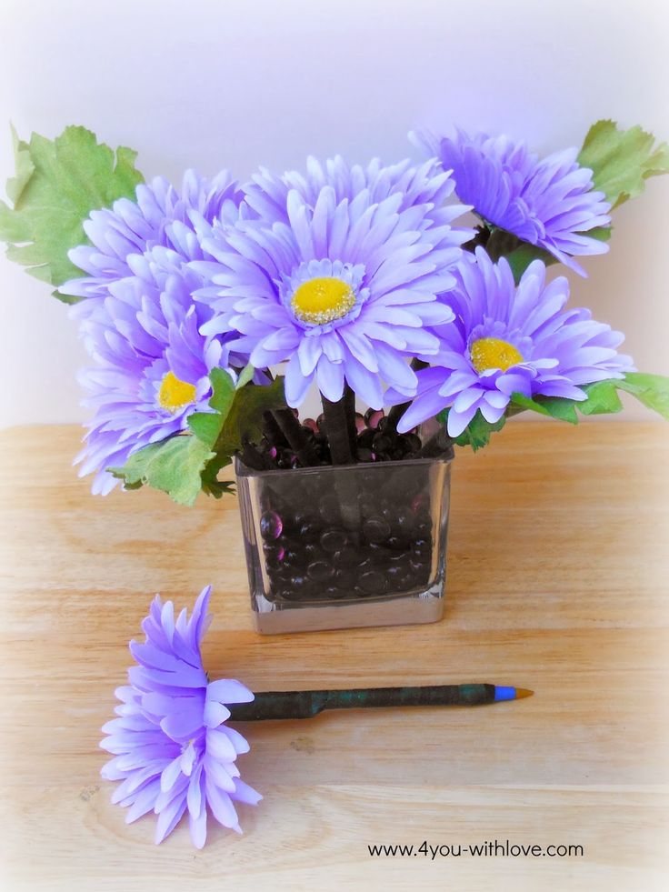 purple flowers in a glass vase with green leaves and pencils on a wooden table