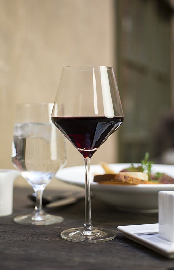 two glasses of red wine are sitting on a table with plates and utensils