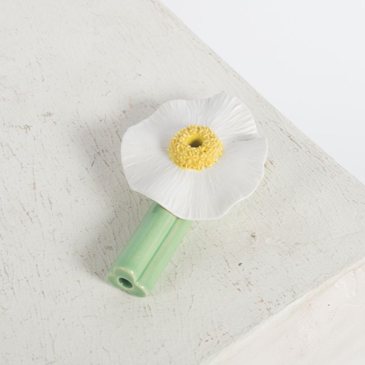 a white flower sitting on top of a wooden table next to a green object with a yellow center