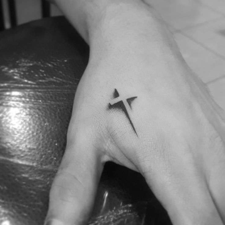 a person's hand with a small cross tattoo on it