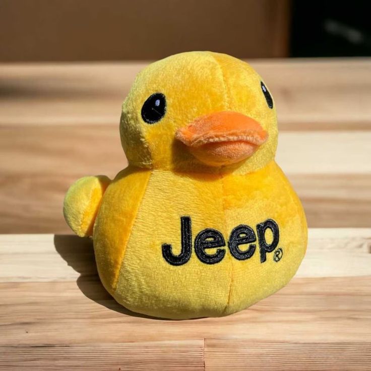 a yellow stuffed toy duck with the word jeep on it's chest sitting on a wooden surface