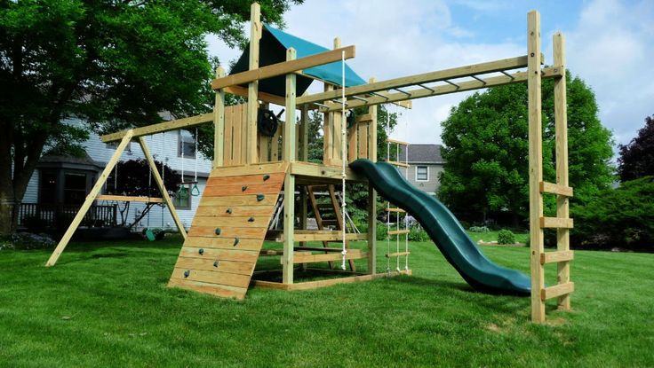 a wooden playset with a slide and climbing frame in the grass next to a house