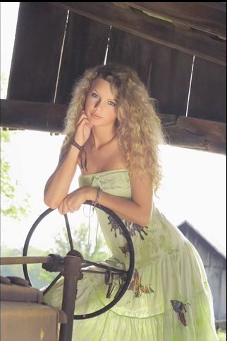 a beautiful woman in a green dress leaning on a steering wheel