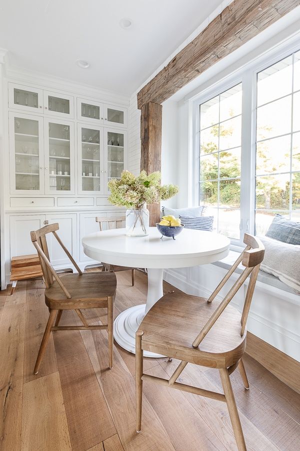 a white table and two chairs in a room with wood flooring, windows, and built - in cabinets