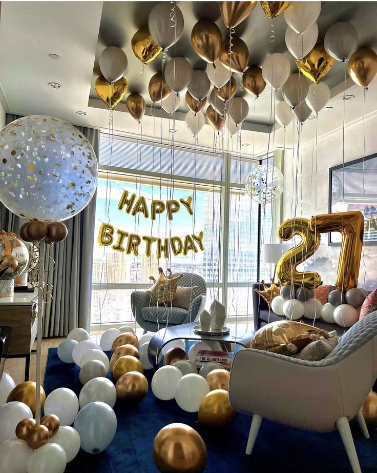 a room filled with balloons and furniture in front of a large window that says happy birthday