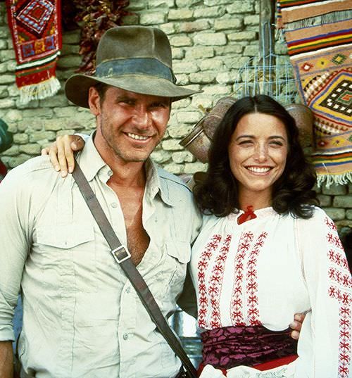 a man and woman standing next to each other in front of a brick wall with colorful rugs on it