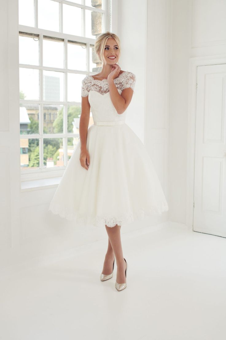 a woman standing in front of a window wearing a white dress