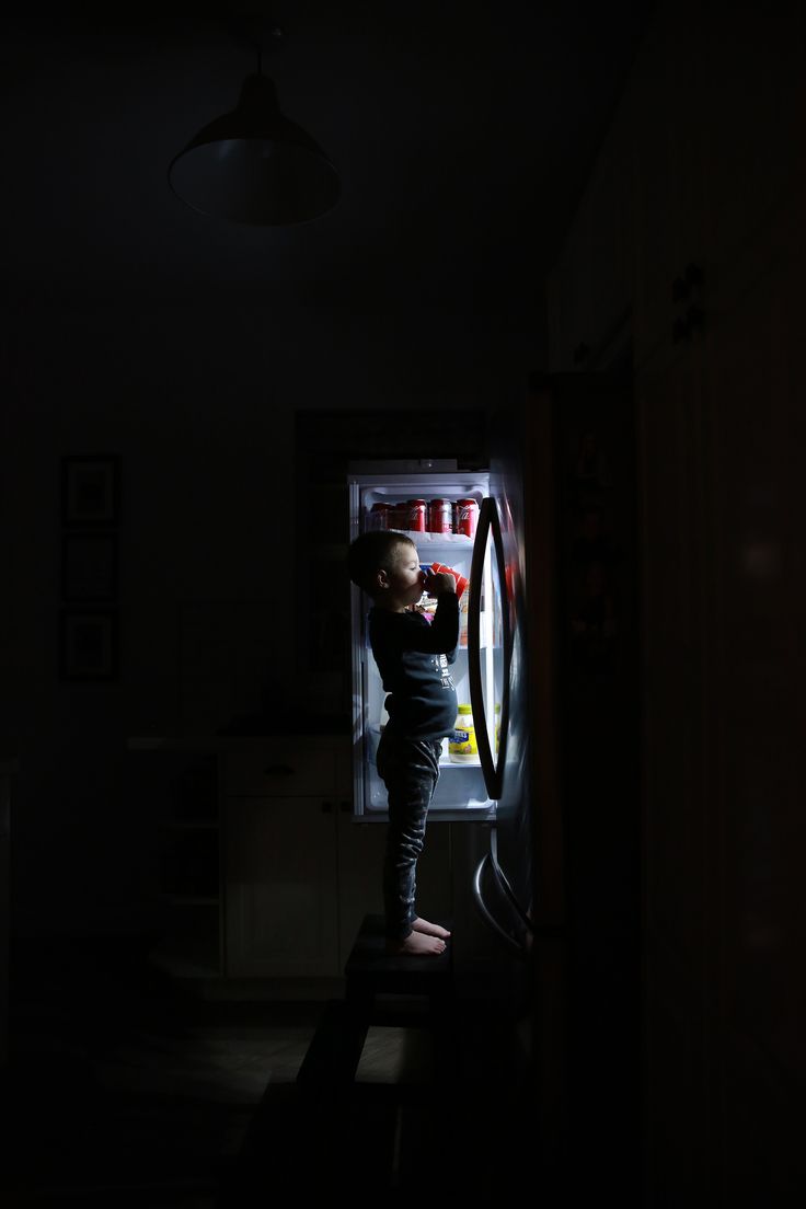 a person standing in front of an open refrigerator with the door wide open at night