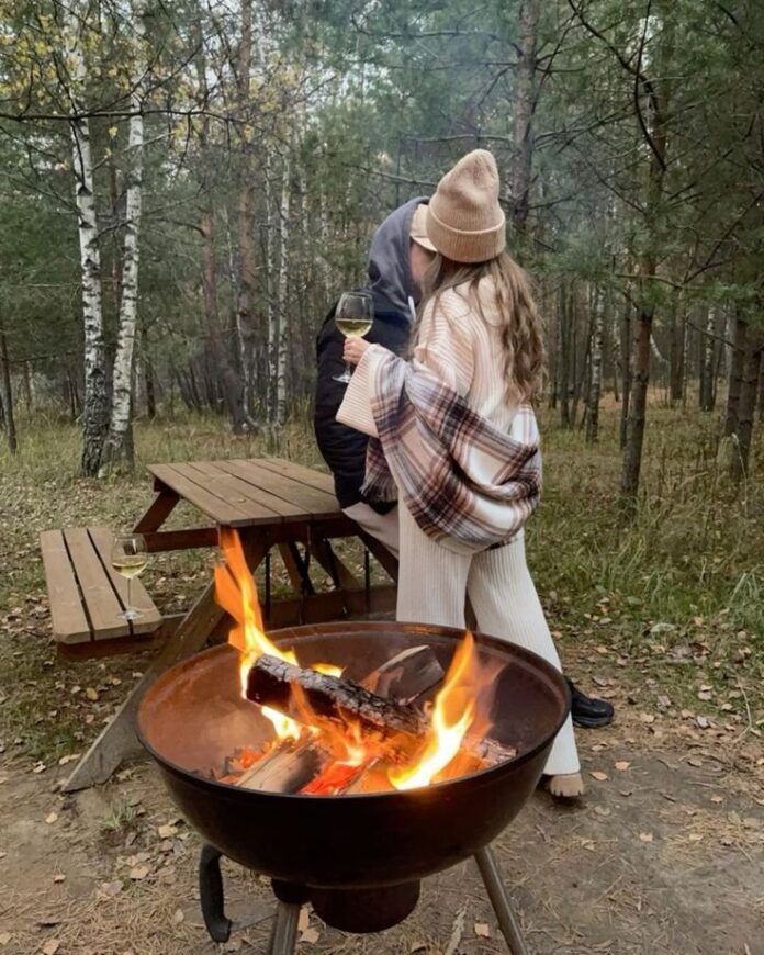 a man and woman standing next to an open fire pit