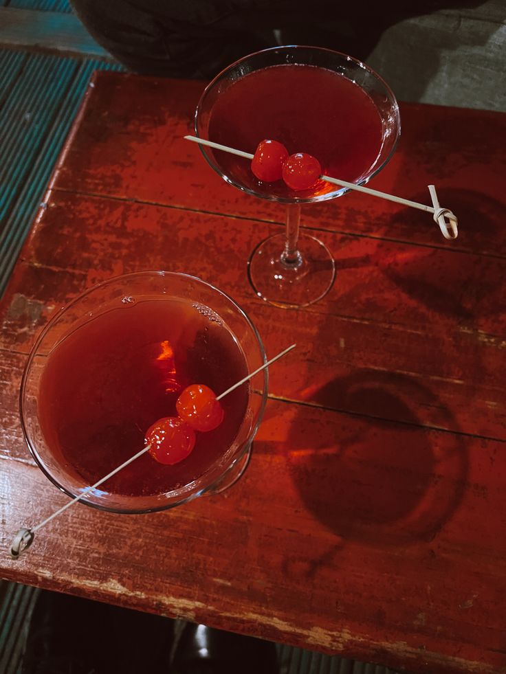 two glasses filled with red liquid sitting on top of a wooden table next to each other