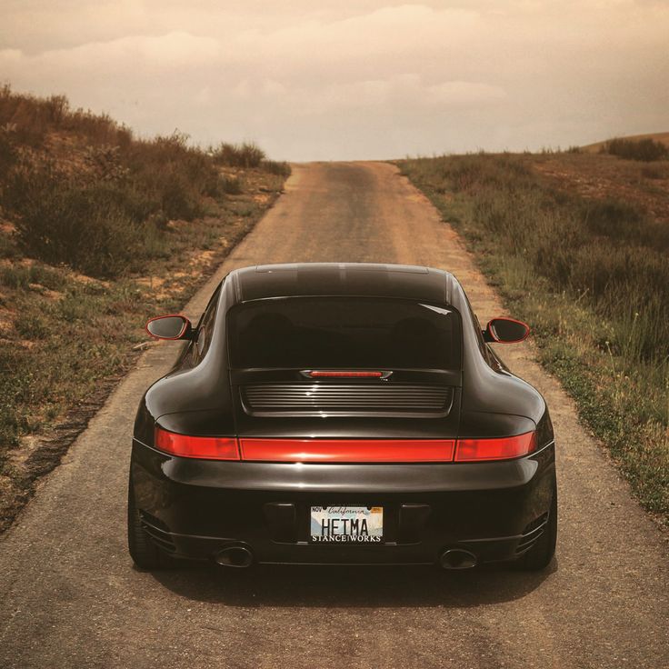 a black sports car parked on the side of a dirt road next to a field