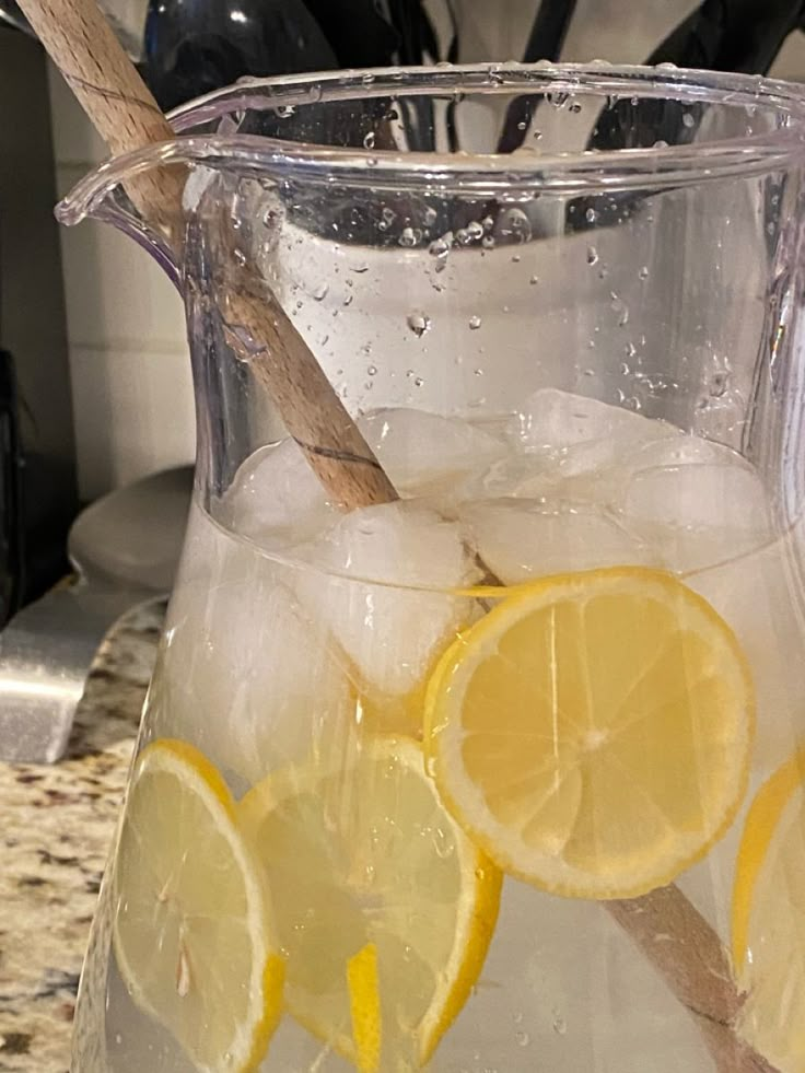 a pitcher filled with ice and lemons sitting on top of a counter next to a wooden spoon