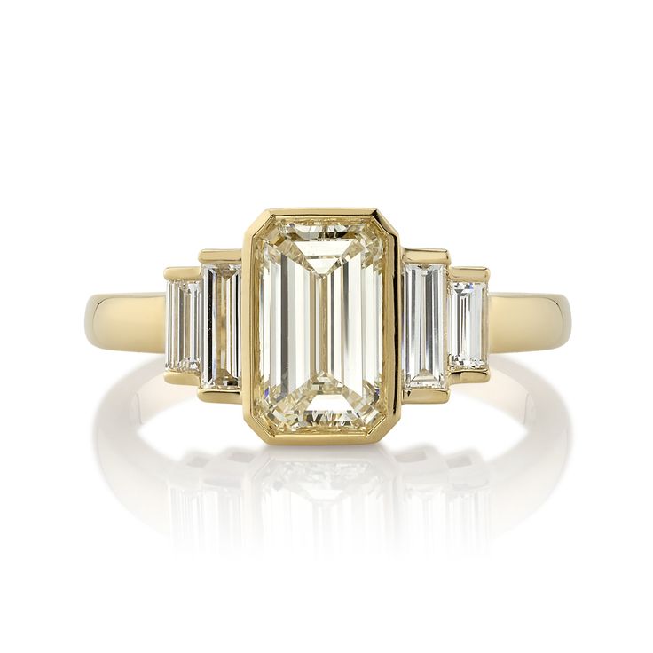 an emerald and diamond ring with three baguets on the side, set in yellow gold