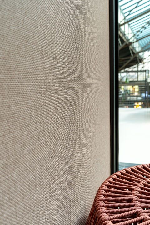 a red chair sitting next to a window in front of a wall covered with fabric