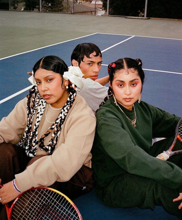 three people sitting on the ground with tennis rackets