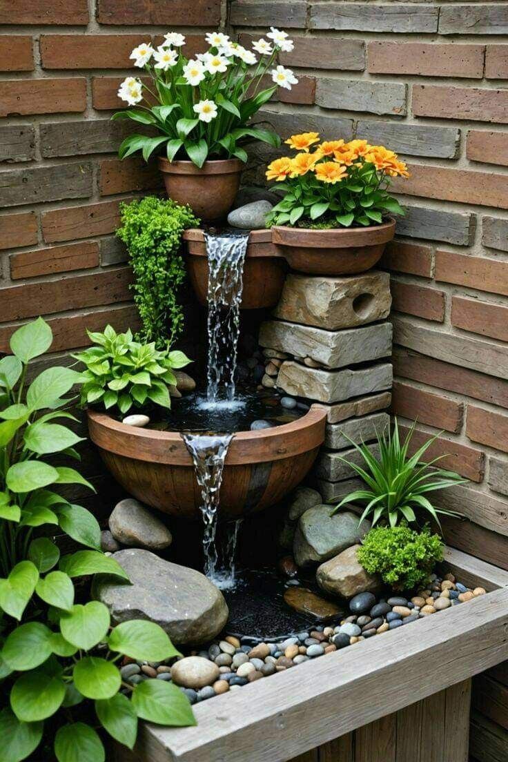 an outdoor fountain surrounded by potted plants and rocks in front of a brick wall