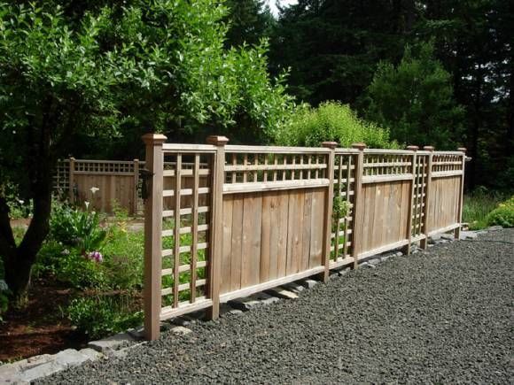 a wooden fence in the middle of a graveled area with trees and bushes behind it