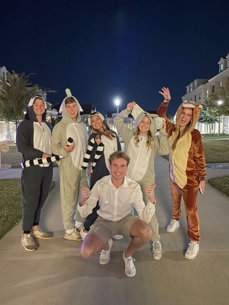 a group of people in animal costumes posing for a photo on a sidewalk at night