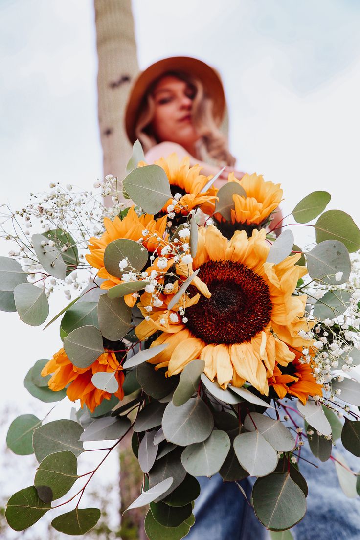 a woman holding a bouquet of sunflowers in front of a tall tree with leaves