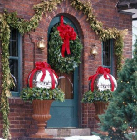 two christmas wreaths sitting on top of large planters in front of a brick building