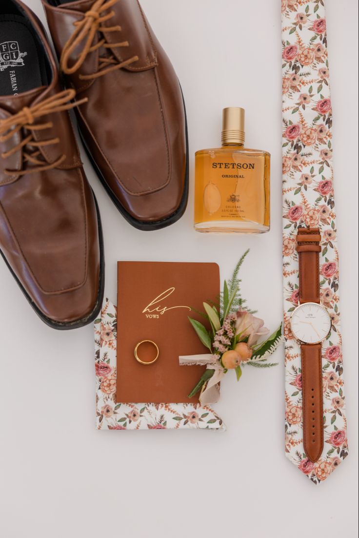 a pair of brown shoes next to a notepad, watch and ring on a white surface