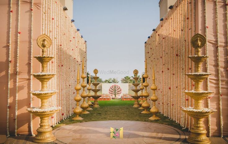 the entrance to an outdoor wedding venue with gold pillars and flowers on it's side