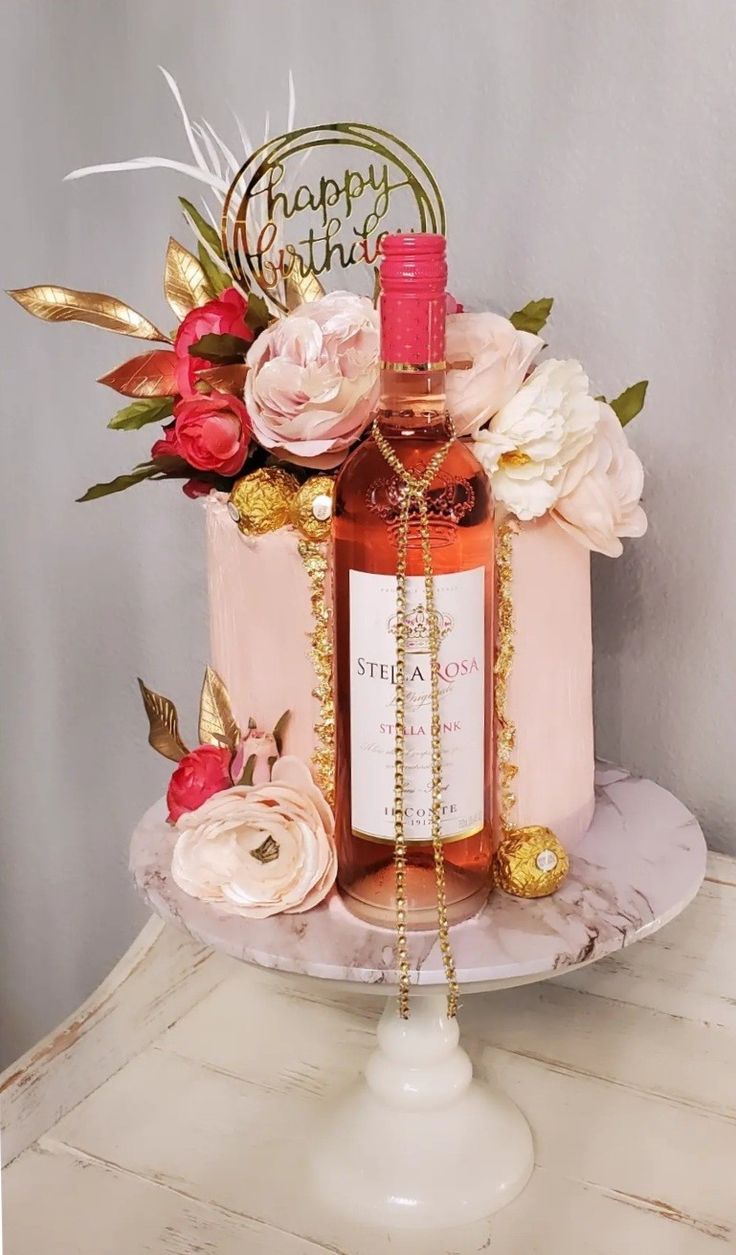 a birthday cake decorated with flowers and a bottle of booze on a white pedestal