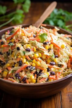 a salad with carrots, corn and black beans in a brown bowl on a wooden table