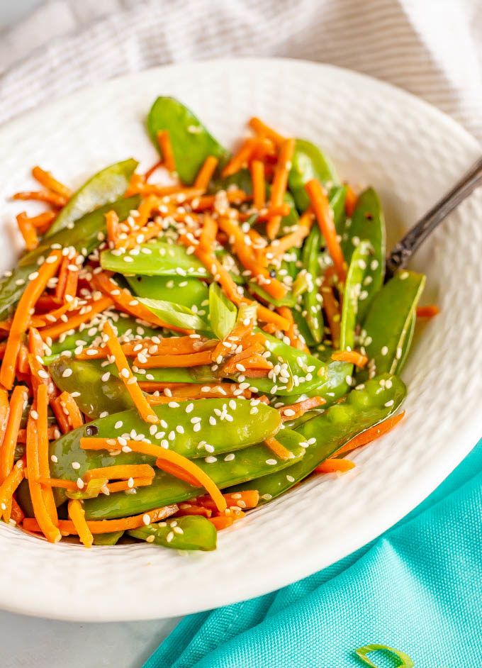 a white bowl filled with green beans and carrots covered in sesame seeds, topped with sesame seeds