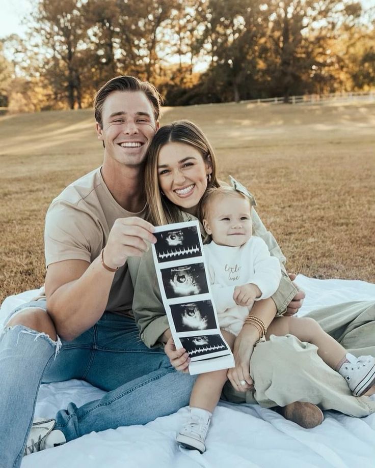 a man and woman sitting on the ground with a baby in their lap holding up a photo