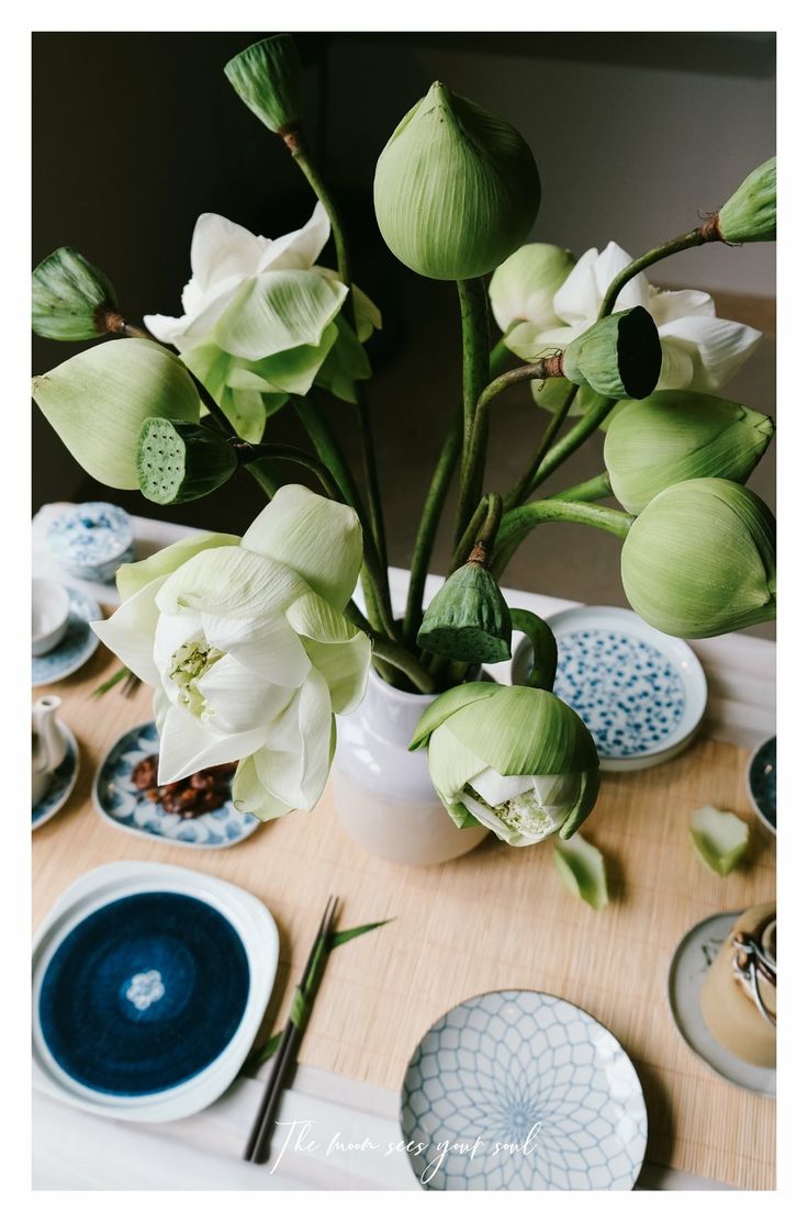 there is a vase with white flowers in it and plates on the table next to it