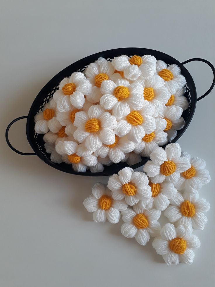 white and yellow crocheted flowers in a black bowl on a table top with string