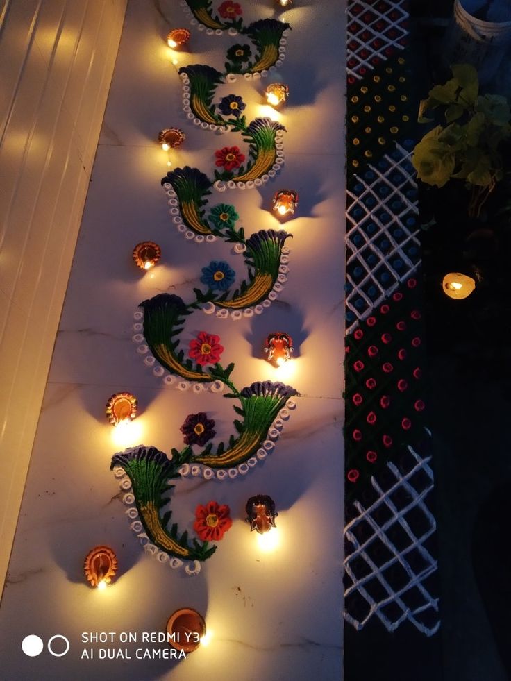 some candles are lit up on the floor in front of a wall with flowers and leaves