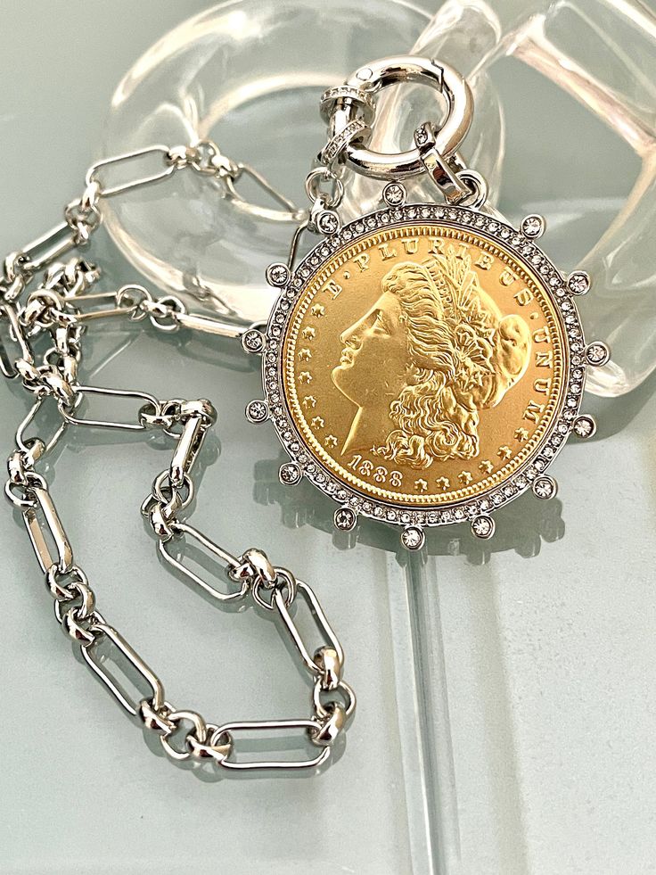 Beautiful reproduction vintage Gold coin pendant, Morgan Peace Dollar coin in a silver bezel with cubic zirconia stones. The bale attached to the coin is also encrusted with CZ stones. The coin is 22k gold plated and elegantly hangs from a multi link Rhodium plated brass chain and a spring lock CZ clasp The spring lock closure not only makes it easy to open and close the necklace for those with difficulty but adds to the creativity of the jewelry piece. Will enhance any outfit. Jeans to the litt