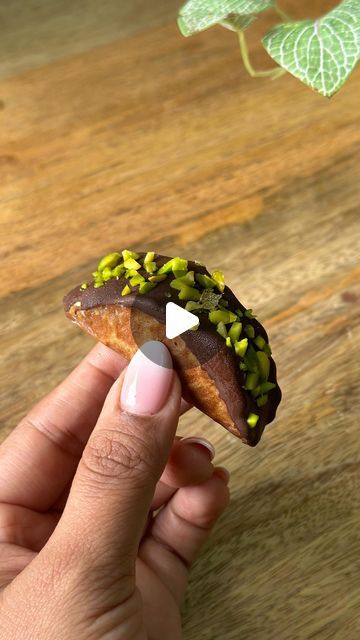 a hand holding a tiny piece of food on top of a wooden table next to a plant