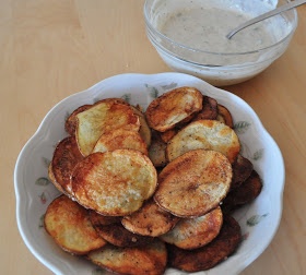 a white bowl filled with fried potatoes next to a container of ranch dressing on a wooden table