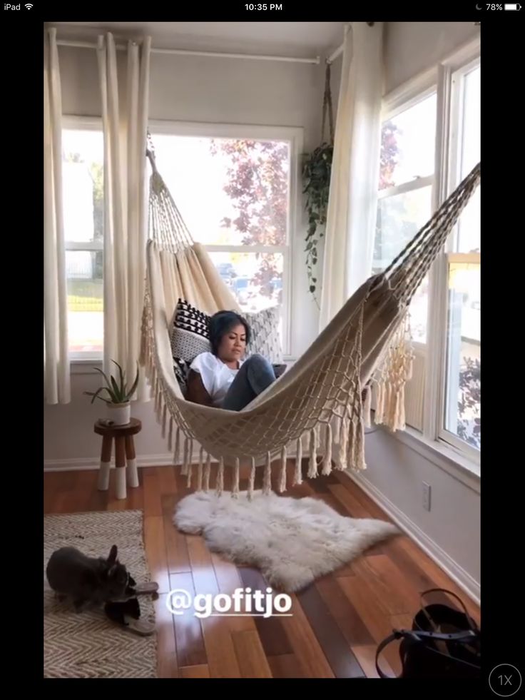 a woman sitting in a hammock with her cat on the floor next to her